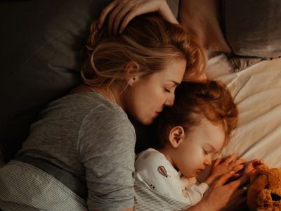 Una mamá y su hija acurrucadas en la cama; la crianza positiva puede ayudar a los niños a superar los problemas de sueño.