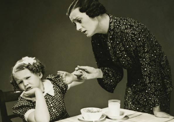 black and white 1930s mother tries to make child eat dinner